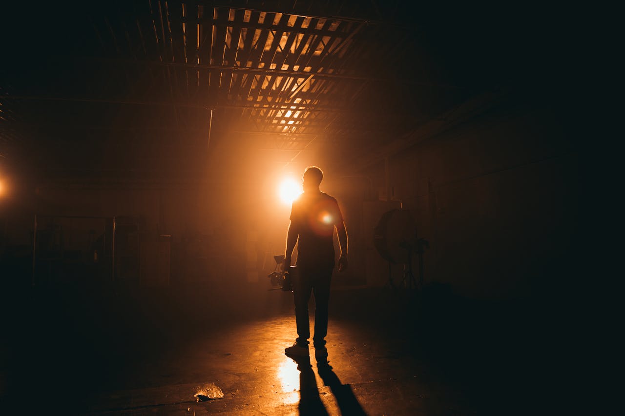 Dramatic silhouette of a cinematographer holding equipment on a dimly lit film set.